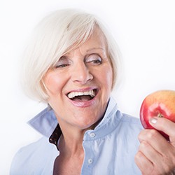 woman holding an apple and maintaining her dental implants in Westhampton