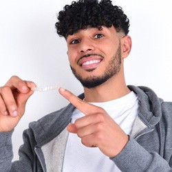 young man smiling and pointing to his Invisalign aligner