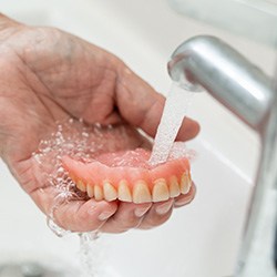 hand rinsing dentures off in the sink