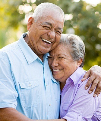 Smiling couple with dental implants in Westhampton hugging outside 