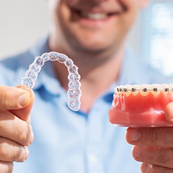 man holding an Invisalign aligner and a model with braces