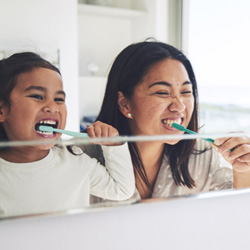 mom and child brushing their teeth in front of a bathroom mirror