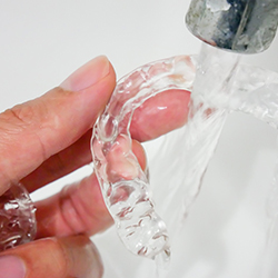hand holding clear Invisalign trays under a faucet with water