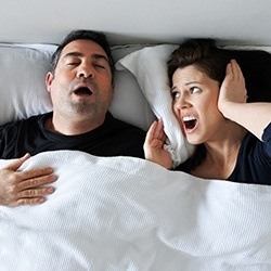 Woman covering ears next to snoring man