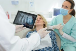 dentist holding a tablet with a dental X-ray on it and talking to a patient