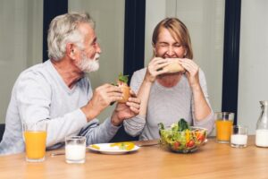 two older adults eating sandwiches and smiling