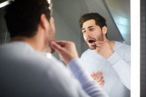 man looking at his teeth in the mirror